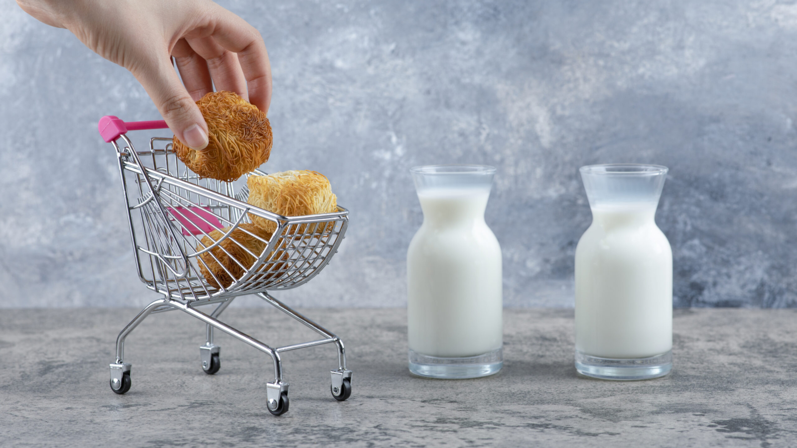 Woman hand taking sweet pastry from small pink cart placed on a marble background. High quality photo